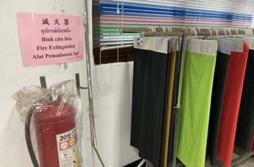 A fire extinguisher mounted on a wall next to multilingual safety instructions and a rack of colorful fabric samples.